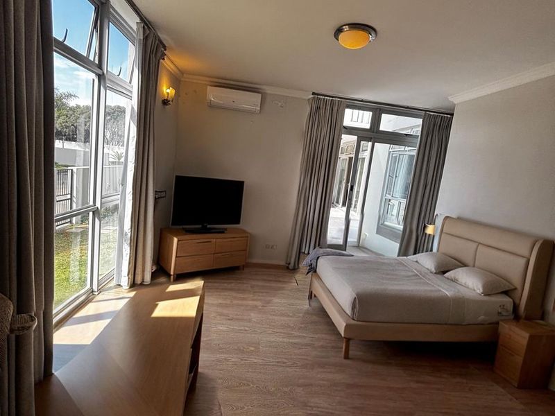 Spacious bedroom featuring laminate flooring, split-system air conditioning, and large windows providing ample natural light and access to the outdoor area.