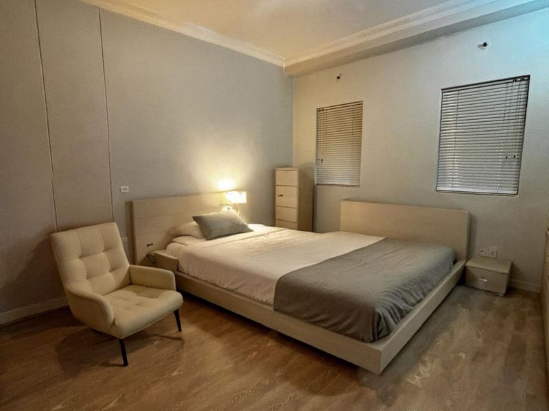 A well-maintained bedroom featuring laminate flooring, neutral wall tones, and dual windows fitted with venetian blinds.