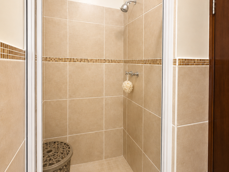A clean, well-maintained shower stall featuring neutral-toned wall and floor tiles with a decorative mosaic accent border.