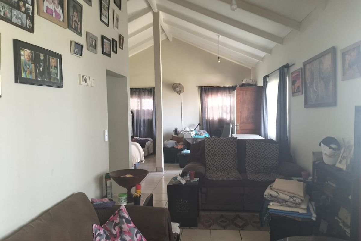 A living room featuring a high vaulted ceiling with exposed rafters and tiled flooring, offering a spacious feel with natural light.