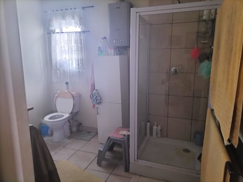 A functional bathroom featuring a shower enclosure, toilet, and wall-mounted gas water heater with tiled flooring and wall finishes.
