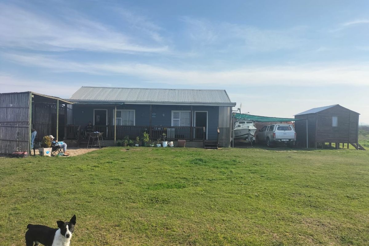 Rear view of a detached house featuring a corrugated metal roof, timber decking, and an attached carport area set on a large grassed plot.