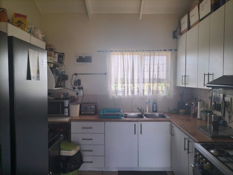 A functional kitchen featuring white cabinetry, laminate countertops, a double basin sink, and a built-in gas hob with an extractor fan.