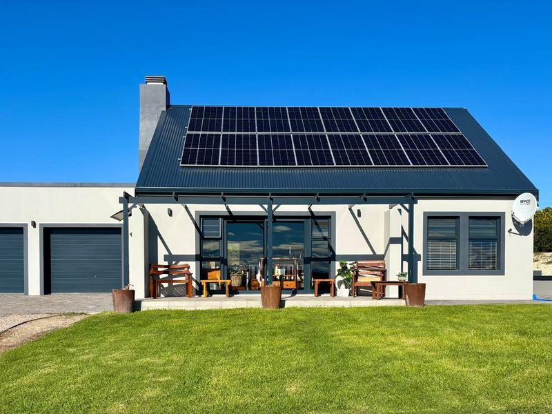 Rear view of a modern home featuring a corrugated metal roof with integrated solar panels, a covered patio, and an attached double garage.
