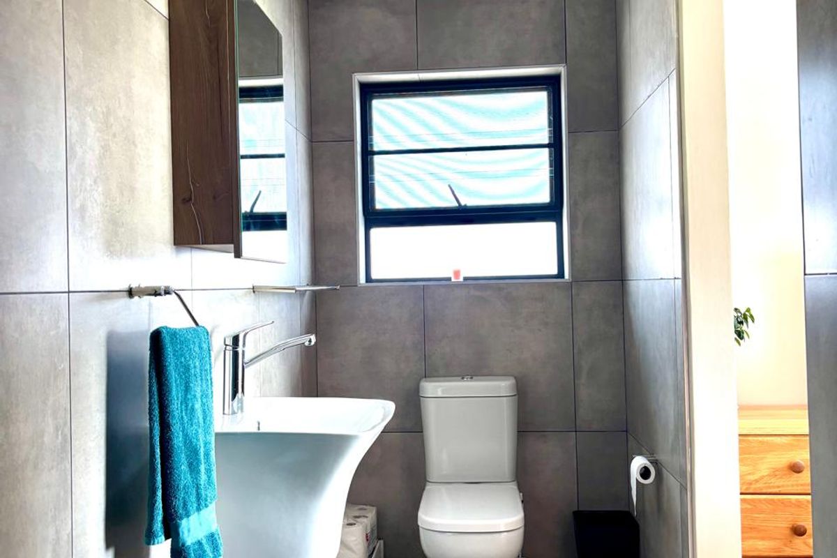 A modern bathroom featuring large-format grey wall tiles, a wall-mounted basin, a toilet, and a clean tongue and groove ceiling.