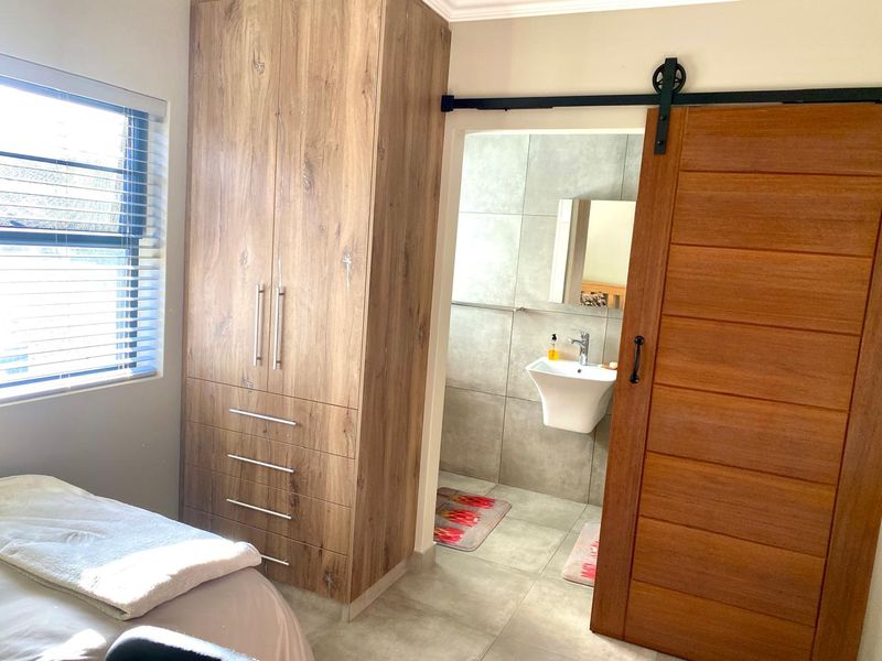Bedroom featuring a built-in wooden wardrobe and a sliding barn door leading to a modern en-suite bathroom with a wall-mounted basin.
