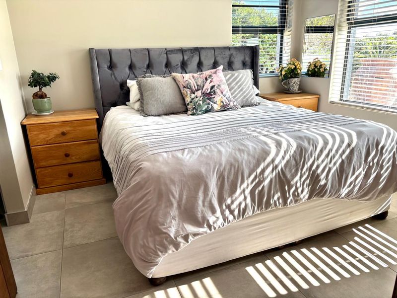 A well-lit bedroom featuring neutral tiled flooring and venetian blinds, providing a clean and comfortable living space.