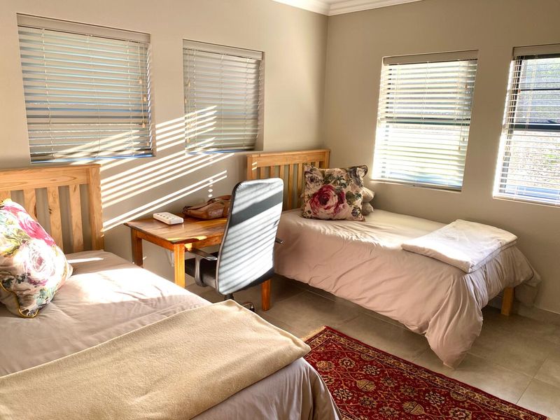 A bright bedroom featuring tiled flooring, neutral wall tones, and multiple windows fitted with venetian blinds, offering a clean and functional living space.