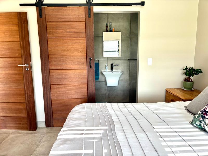 A well-maintained bedroom featuring a modern sliding barn door leading to an en-suite bathroom with a wall-mounted basin and tiled finishes.