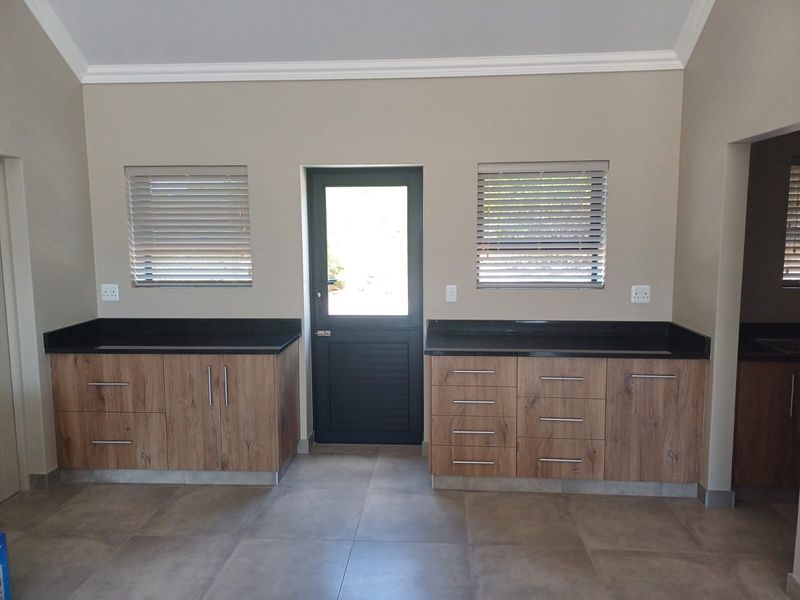 A clean, modern scullery featuring wood-look cabinetry, dark granite countertops, tiled flooring, and direct access to the exterior.