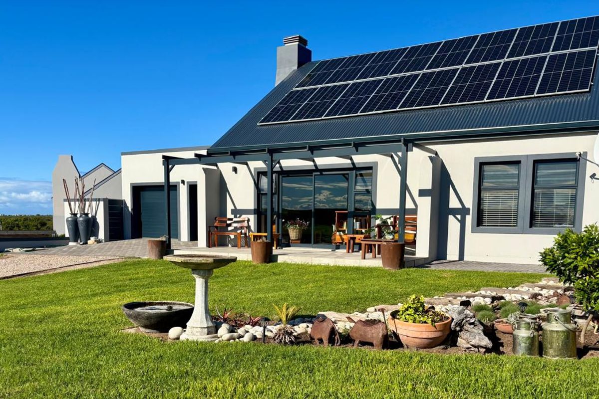 Rear view of a modern home featuring a metal roof with integrated solar panels, a covered patio area, and a well-maintained garden.