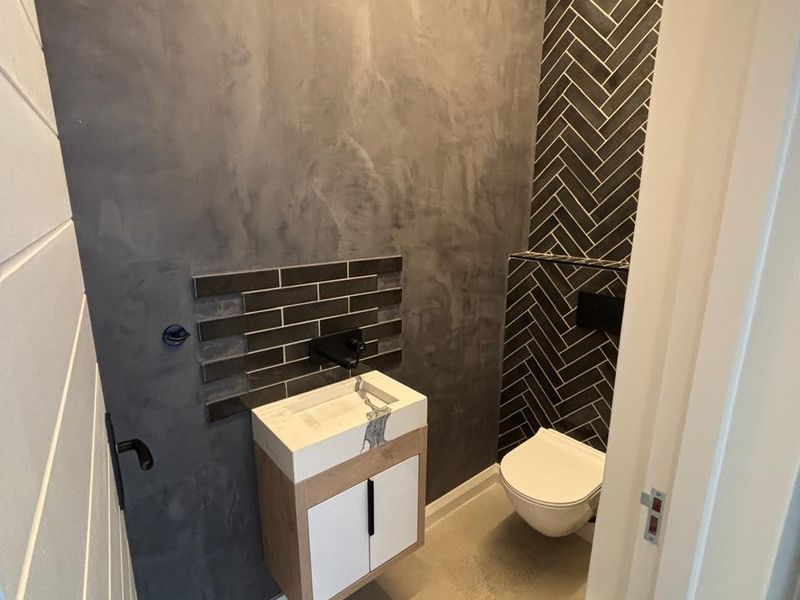 Modern guest bathroom featuring a wall-hung vanity, wall-mounted toilet, stylish herringbone tiling, and contemporary concrete-effect wall finishes.