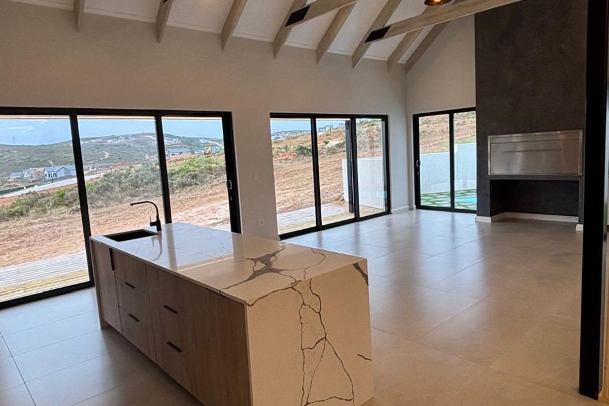 Spacious open-plan living area featuring a modern kitchen island, exposed timber rafters, built-in fireplace, and large sliding doors with scenic views.