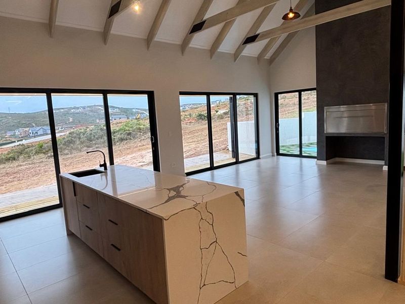 Spacious open-plan living area featuring a modern kitchen island, exposed timber rafters, built-in fireplace, and large sliding doors with scenic views.