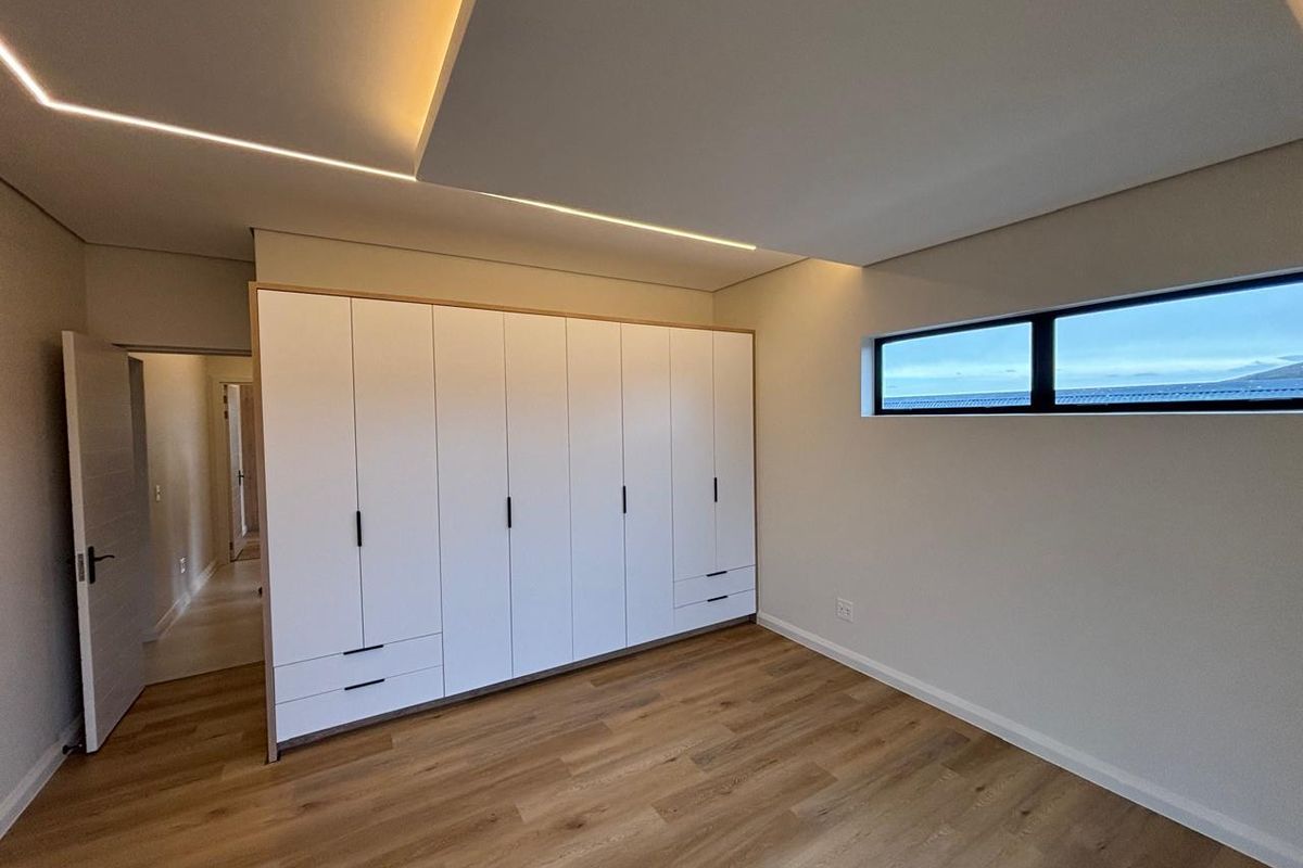 Modern bedroom featuring built-in wardrobes, sleek recessed ceiling lighting, and high-quality laminate flooring with a horizontal window.