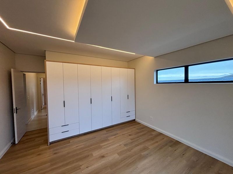Modern bedroom featuring built-in wardrobes, sleek recessed ceiling lighting, and high-quality laminate flooring with a horizontal window.