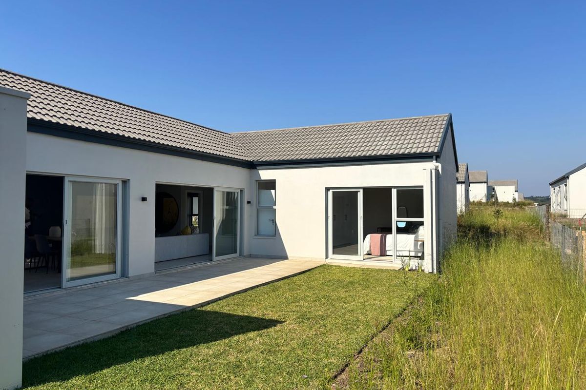 Rear view of a modern house featuring a paved patio, sliding glass doors, and a well-maintained lawn area.