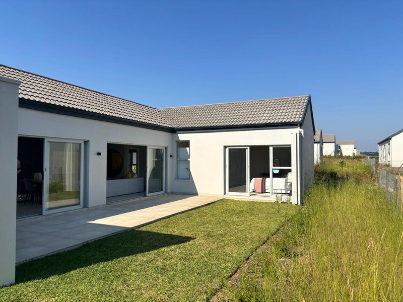 Rear view of a modern house featuring a paved patio, sliding glass doors, and a well-maintained lawn area.