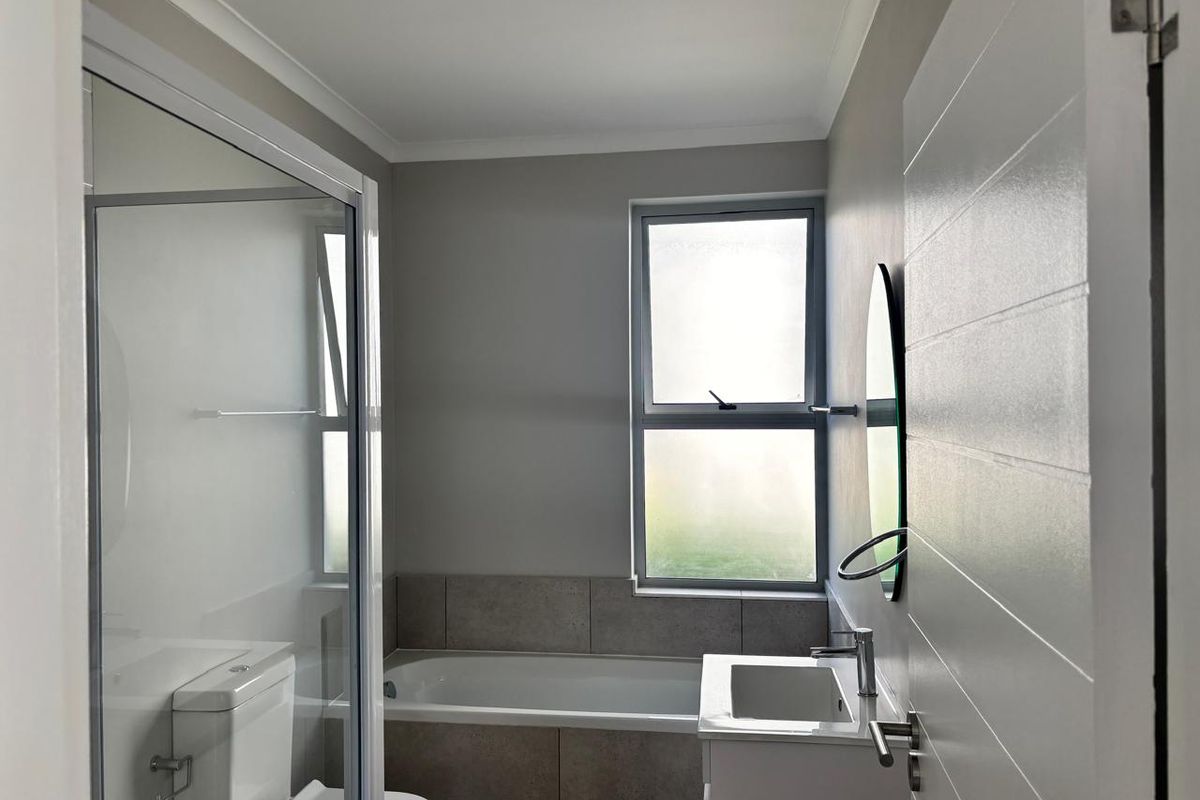 Modern bathroom featuring a glass shower enclosure, built-in bathtub, vanity with basin, and neutral tiling, offering a clean and functional space.