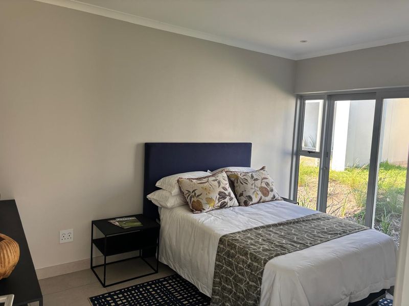 A well-maintained bedroom featuring neutral walls, tiled flooring, and a large sliding glass door providing direct access to the garden area.