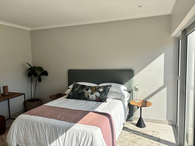 A bright and modern bedroom featuring neutral walls, tiled flooring, recessed downlighting, and a large sliding glass door providing ample natural light.