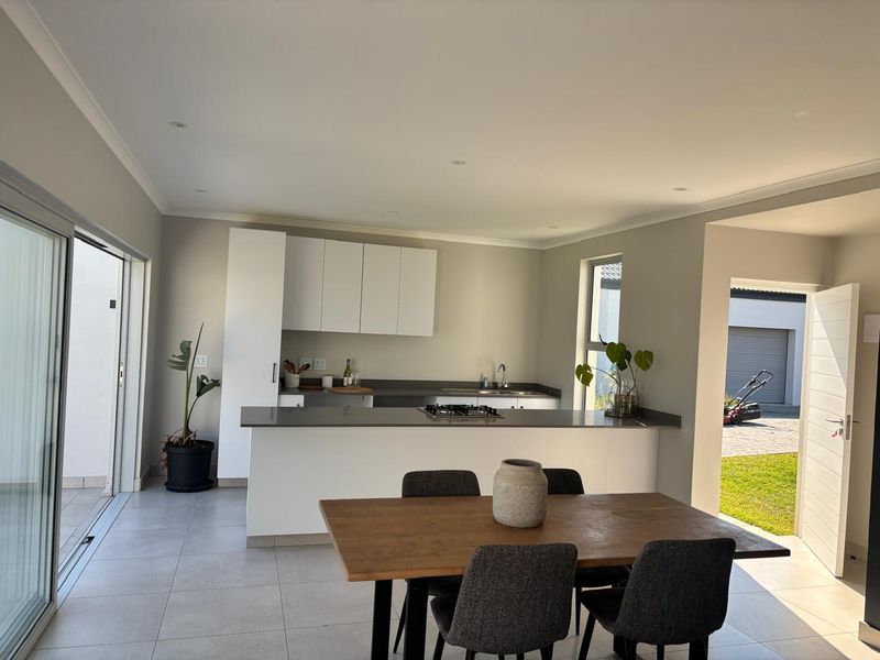 Modern open-plan kitchen and dining area featuring sleek cabinetry, stone countertops, gas hob, and seamless access to the outdoor patio through sliding glass doors.