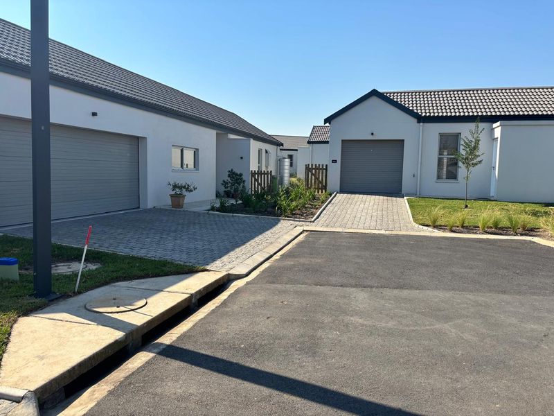 A view of the front exterior of modern residential homes featuring paved driveways, garage doors, and well-maintained tiled roofs in a quiet street setting.