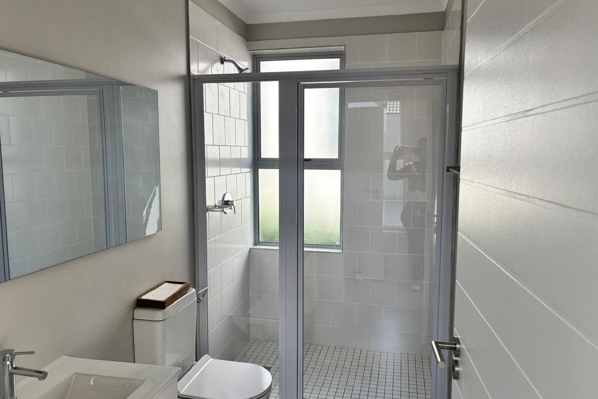 A clean, modern bathroom featuring a glass-enclosed shower, white wall tiling, a vanity basin, and a wall-mounted mirror.