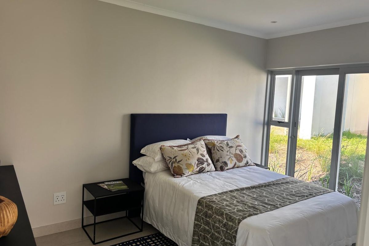 A well-maintained bedroom featuring neutral walls, tiled flooring, and a large sliding glass door providing direct access to the garden area.