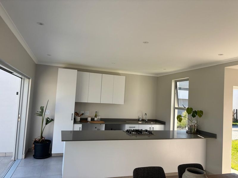 Modern kitchen featuring white cabinetry, dark stone countertops, integrated gas hob, and direct access to the outdoor area through sliding glass doors.