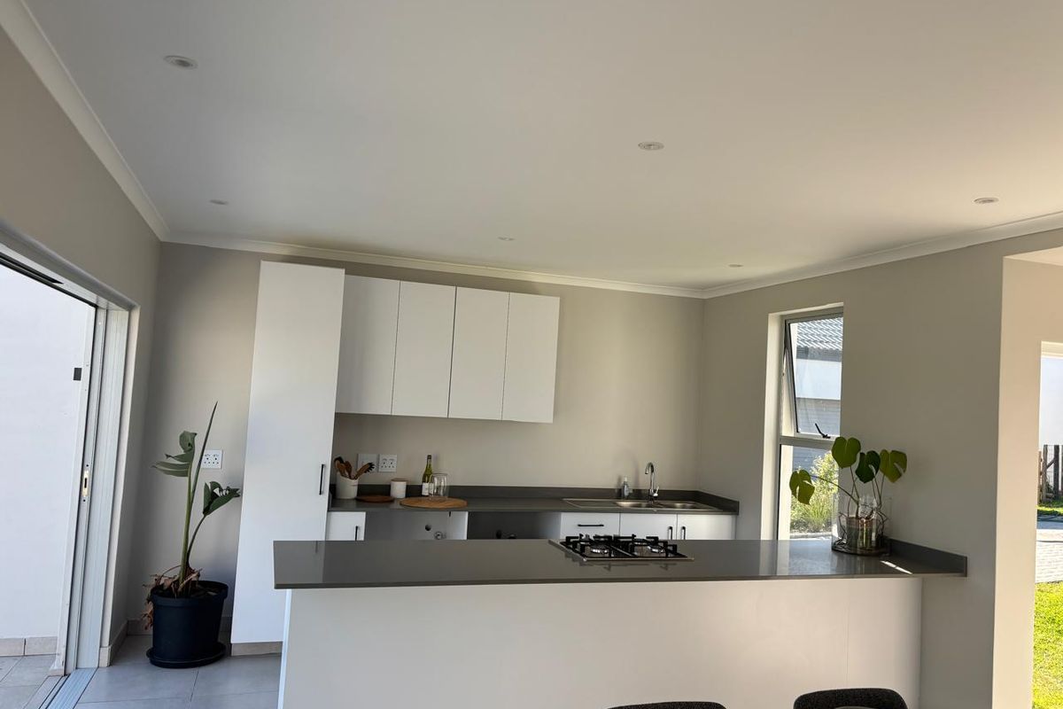 Modern kitchen featuring white cabinetry, dark stone countertops, integrated gas hob, and direct access to the outdoor area through sliding glass doors.