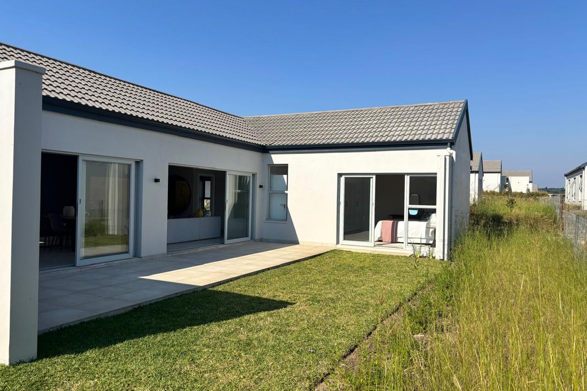 Rear view of a modern house featuring a paved patio area, sliding glass doors, and a well-maintained lawn.