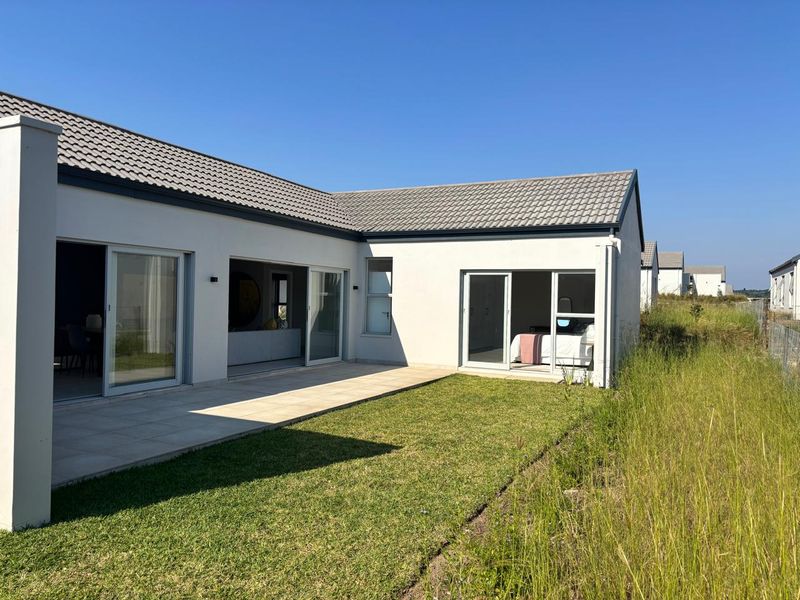 Rear view of a modern house featuring a paved patio area, sliding glass doors, and a well-maintained lawn.