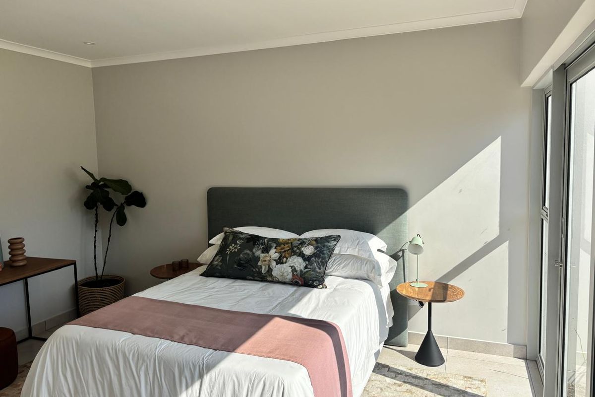 A bright and modern bedroom featuring neutral walls, tiled flooring, recessed downlighting, and a large sliding glass door providing ample natural light.