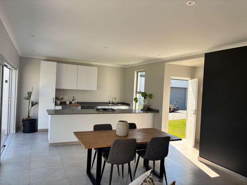 Modern open-plan kitchen and dining area featuring sleek white cabinetry, a gas hob, and large sliding doors leading to the exterior.