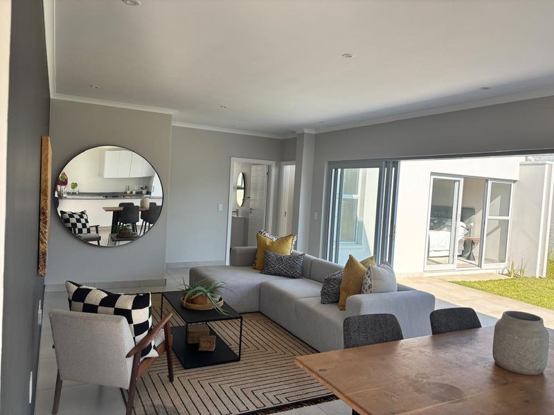 Spacious open-plan living area featuring neutral tones, recessed lighting, and large sliding glass doors that provide seamless access to the outdoor patio and garden.