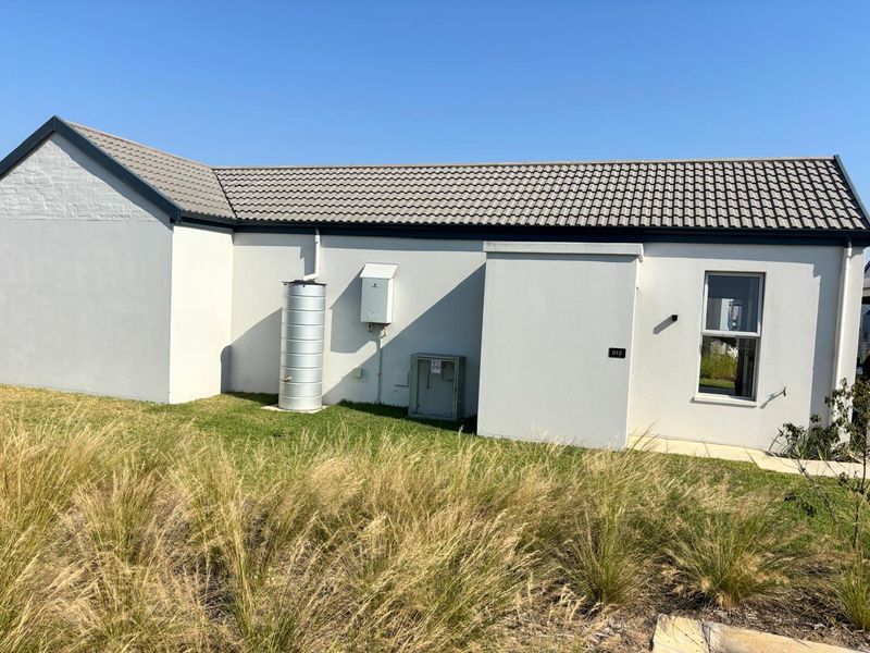Rear exterior view of the property featuring a tiled roof, rainwater tank, gas geyser, and air conditioning unit set against a landscaped garden area.