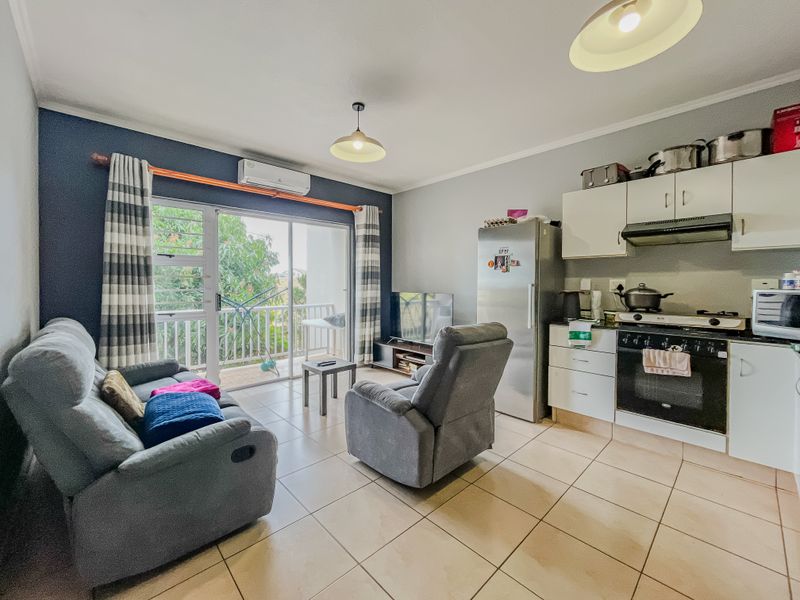 Open-plan living area featuring a compact kitchen with built-in appliances, tiled flooring, and direct access to a balcony through sliding glass doors.