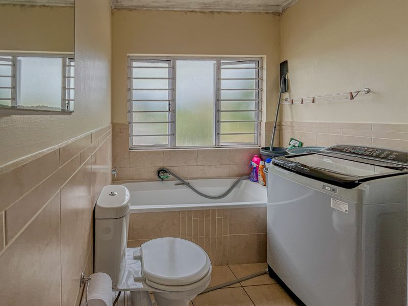 A functional bathroom featuring a built-in bathtub, toilet, and tiled finishes, with visible ceiling wear requiring maintenance.