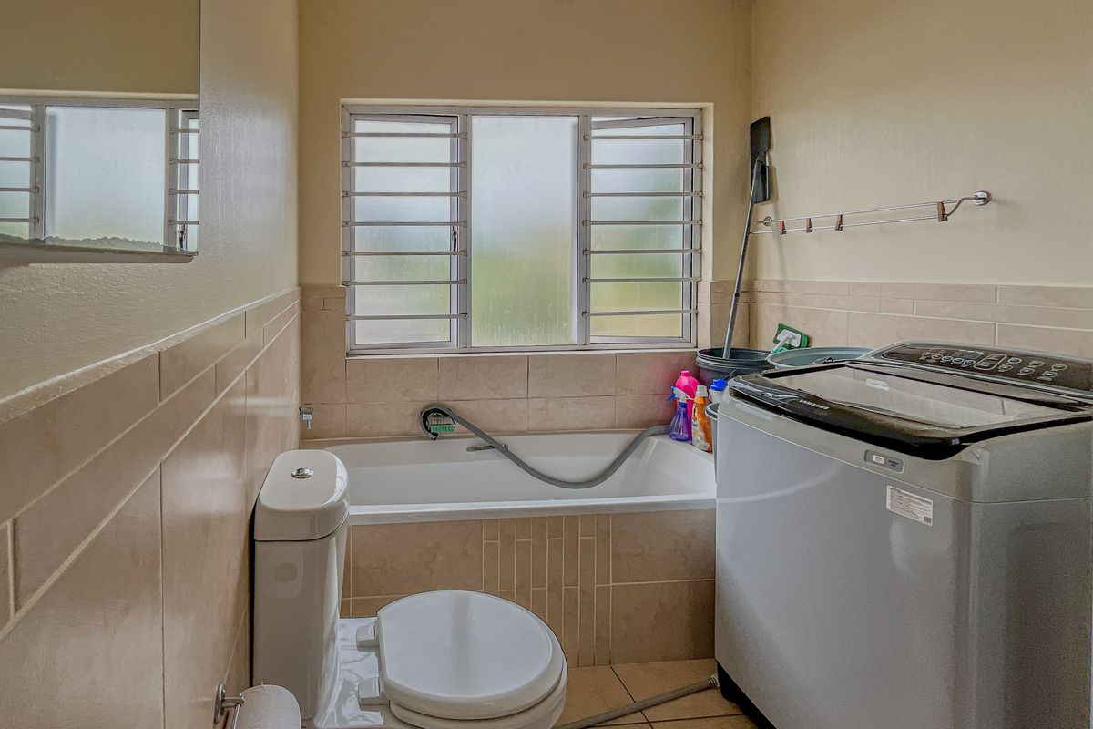 A functional bathroom featuring a built-in bathtub, toilet, and tiled finishes, with visible ceiling wear requiring maintenance.