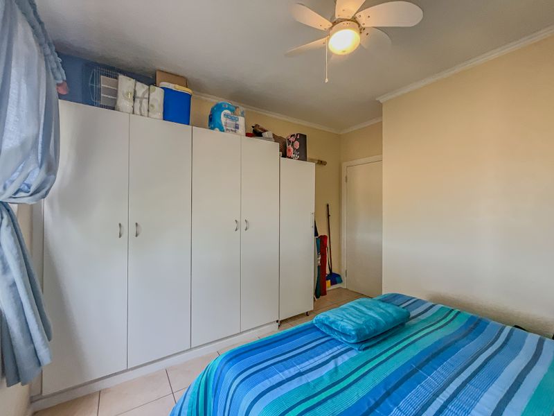 A bedroom featuring built-in cupboards, a ceiling fan, and tiled flooring.