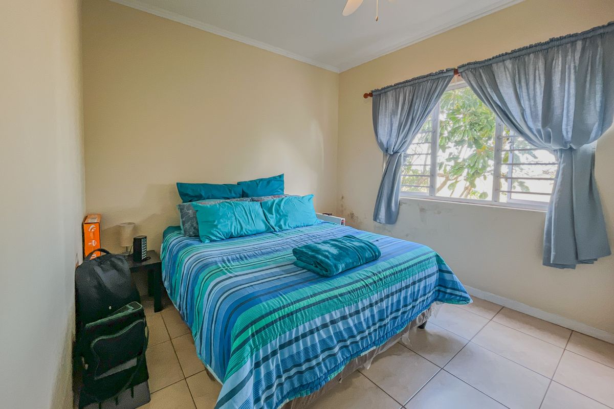 A bedroom featuring tiled flooring, a ceiling fan, and a window with natural light. Visible damp damage is present on the wall below the window.