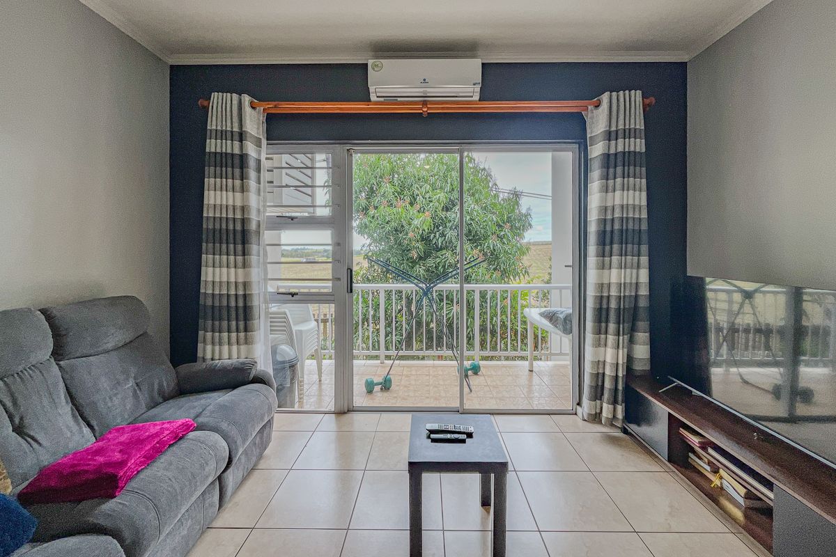 A comfortable living room featuring tiled floors, a wall-mounted air conditioner, and large sliding glass doors that open onto a private balcony.