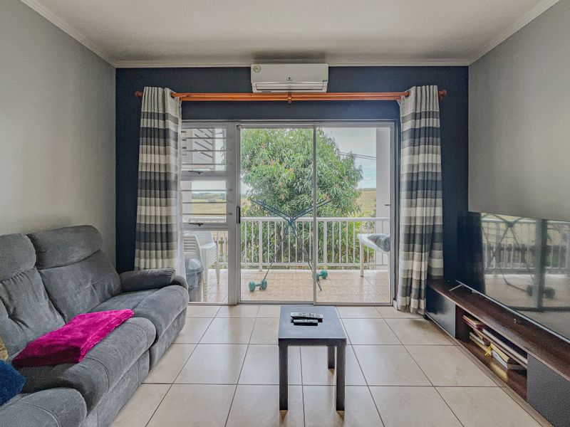 A comfortable living room featuring tiled floors, a wall-mounted air conditioner, and large sliding glass doors that open onto a private balcony.