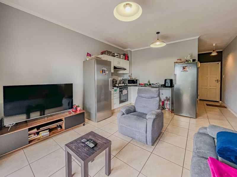 Open-plan living area featuring tiled flooring and a compact kitchen corner with built-in cabinetry, oven, and extractor fan.