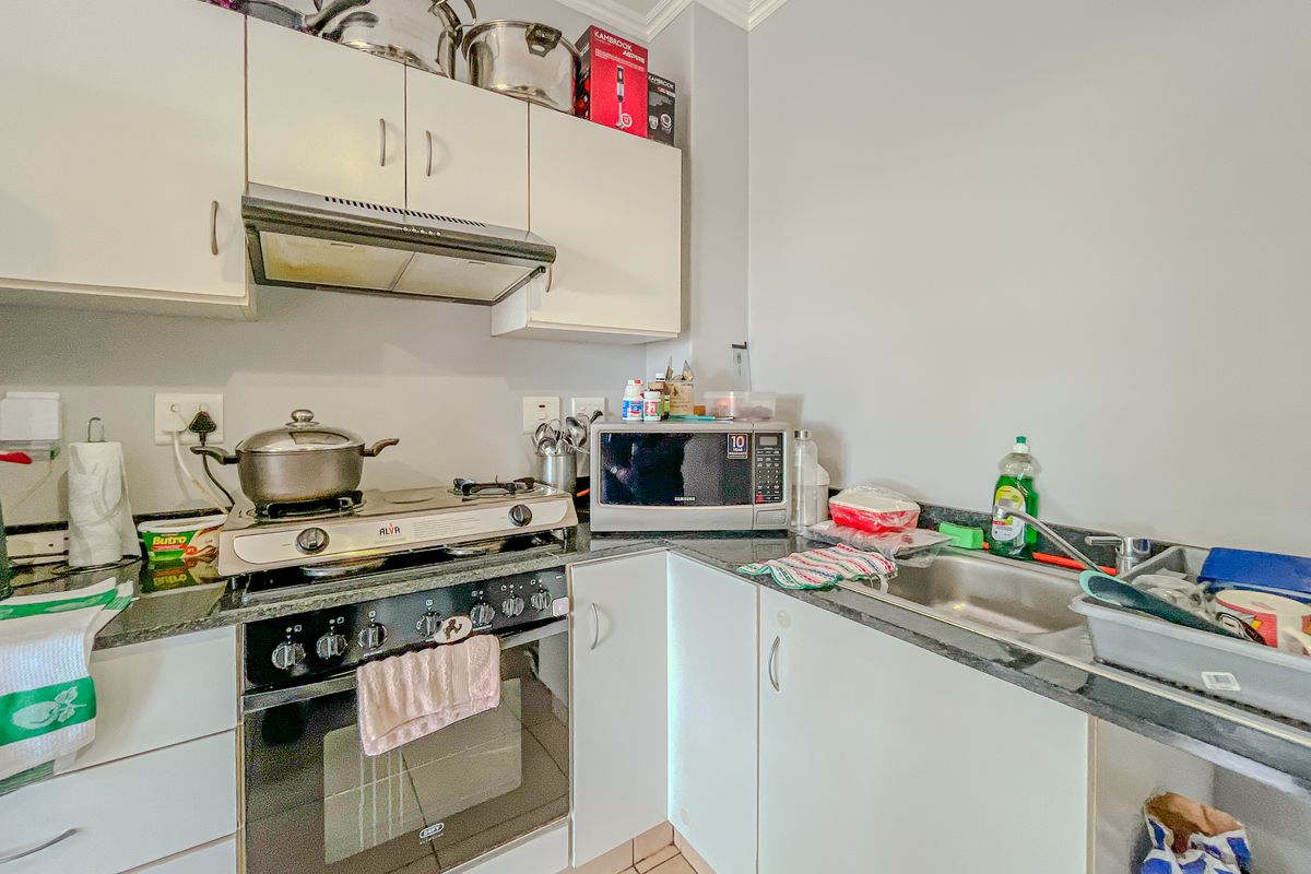 Compact kitchen featuring built-in oven, gas hob, extractor fan, granite countertops, and stainless steel sink with ample storage cabinetry.