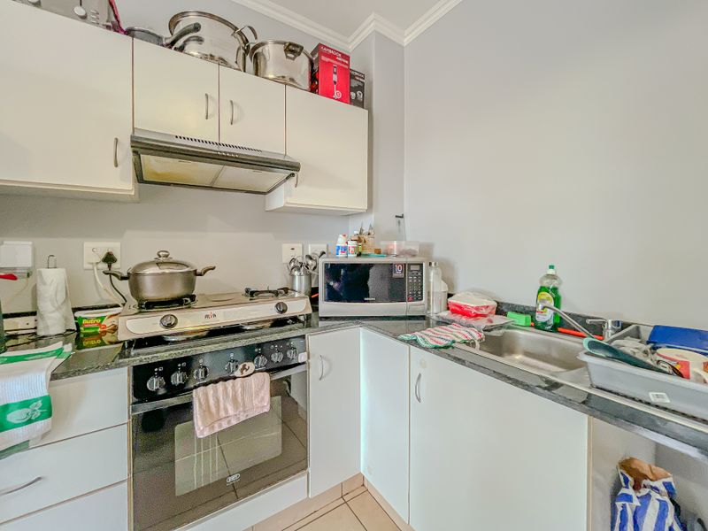Compact kitchen featuring built-in oven, gas hob, extractor fan, granite countertops, and stainless steel sink with ample storage cabinetry.