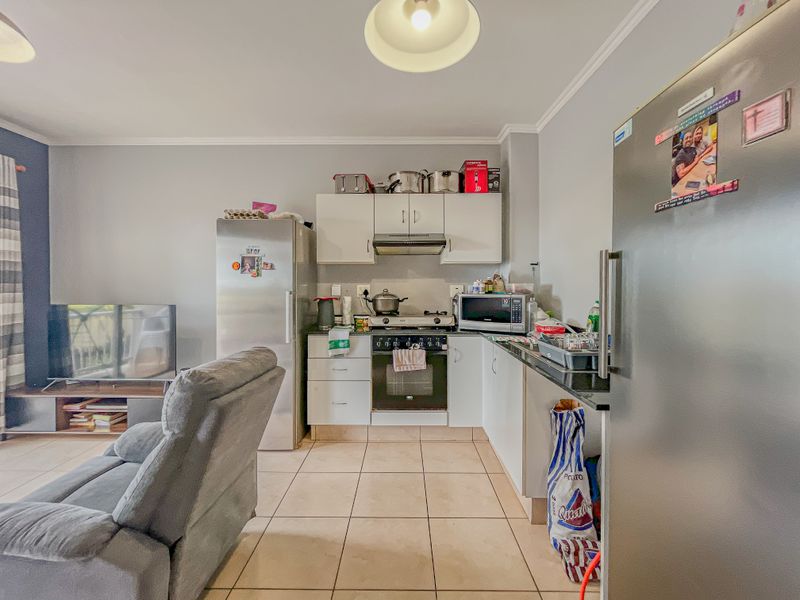 Open-plan living area featuring a functional kitchen with built-in cabinetry, gas hob, and oven, seamlessly flowing into the adjacent living space with tiled flooring.