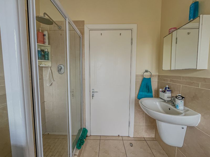 A functional bathroom featuring a glass-enclosed shower, pedestal basin, and wall-mounted medicine cabinet with neutral tiled finishes.