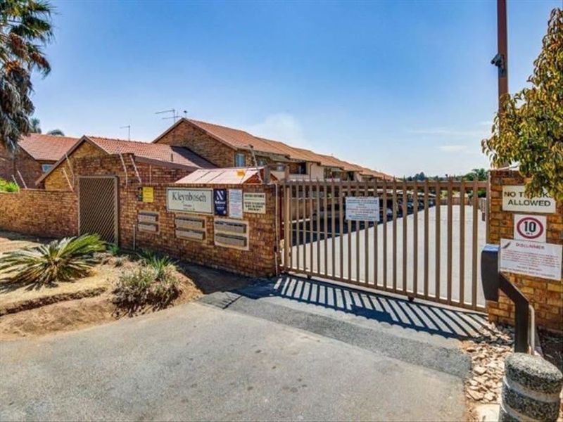 Front entrance view of the townhouse complex featuring a secure automated sliding gate, brick boundary wall with electric fencing, and paved driveway access.